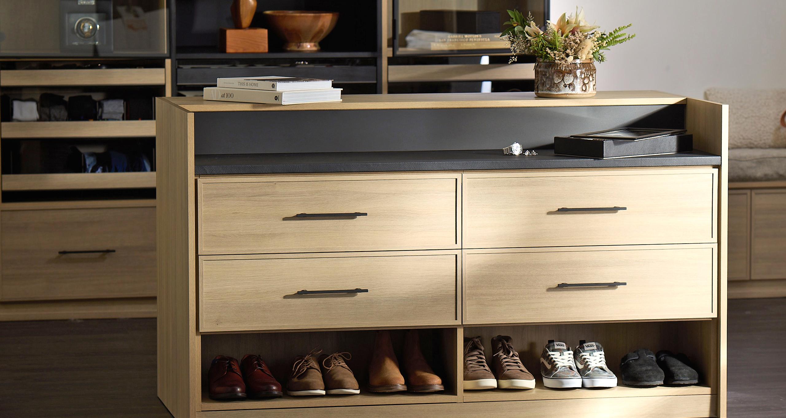 California Closets sustainable light wood island with custom drawers, shoe cubbies, and dark countertop