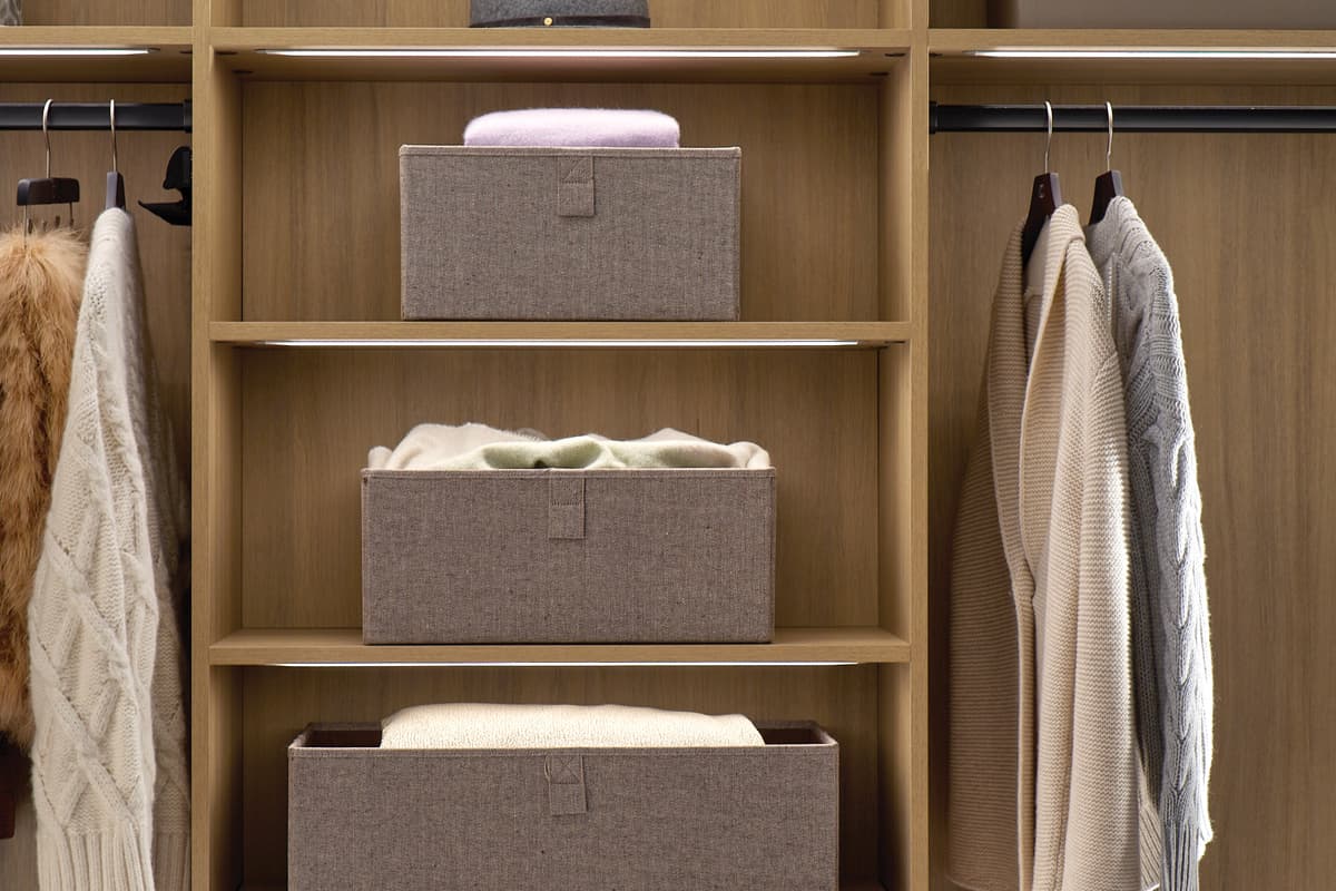 Closet with open shelving and LED lighted clothes rods in natural wood grain finish by California Closets