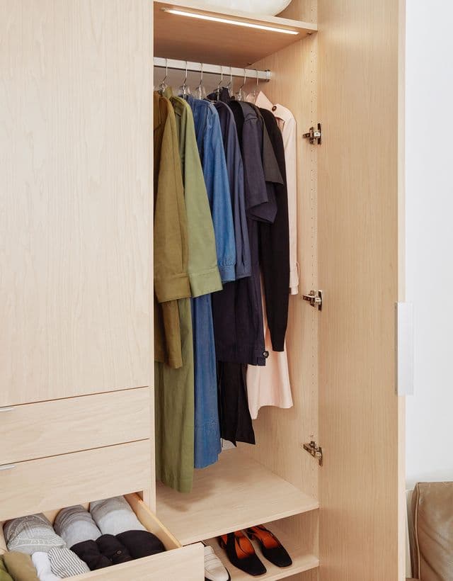 Wardrobe closet opened to show drawers and hanging clothes in a natural wood grain finish by California Closets