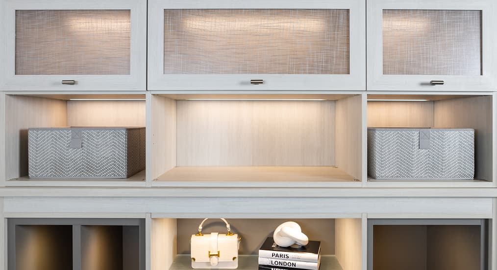 Custom closet cabinetry featuring energy-efficient integrated LED lighting, textured cabinet doors, and open shelf storage.