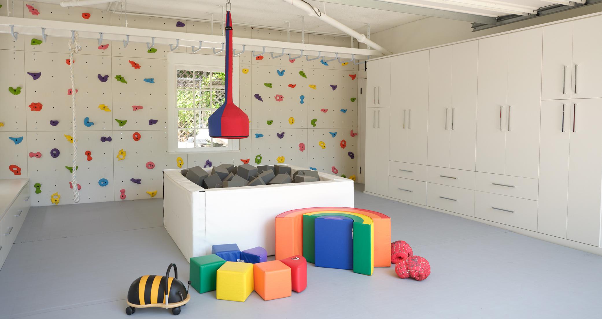 Área de juegos diseñada para un garaje reformado con gabinetes personalizados, estanterías, muro para escalar y gimnasio en la jungla por California Closets