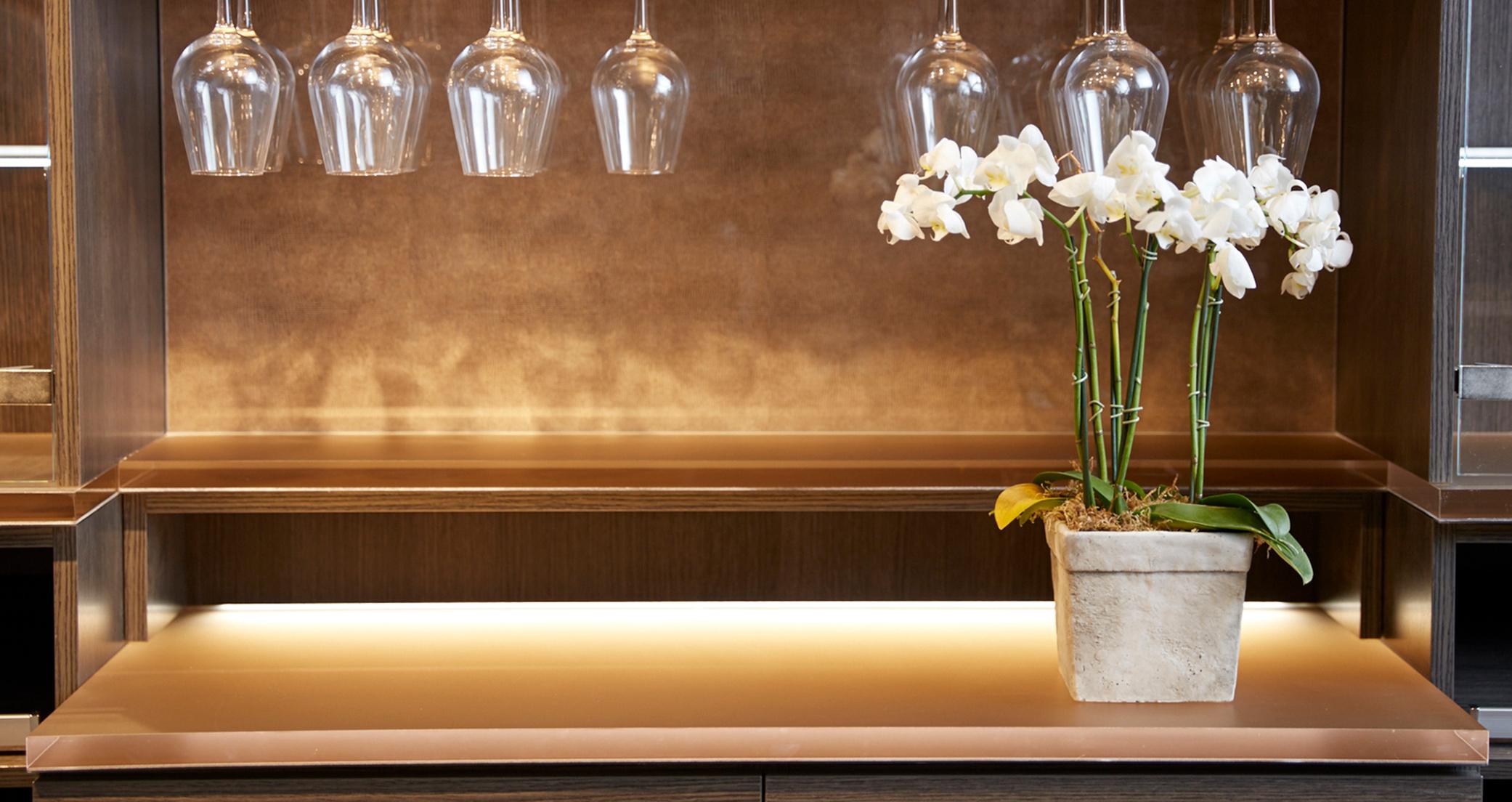 Detalles de almacenamiento de cristalería para bar de vinos en el hogar con diseño de ecoresina en la pared trasera e iluminación LED de California Closets