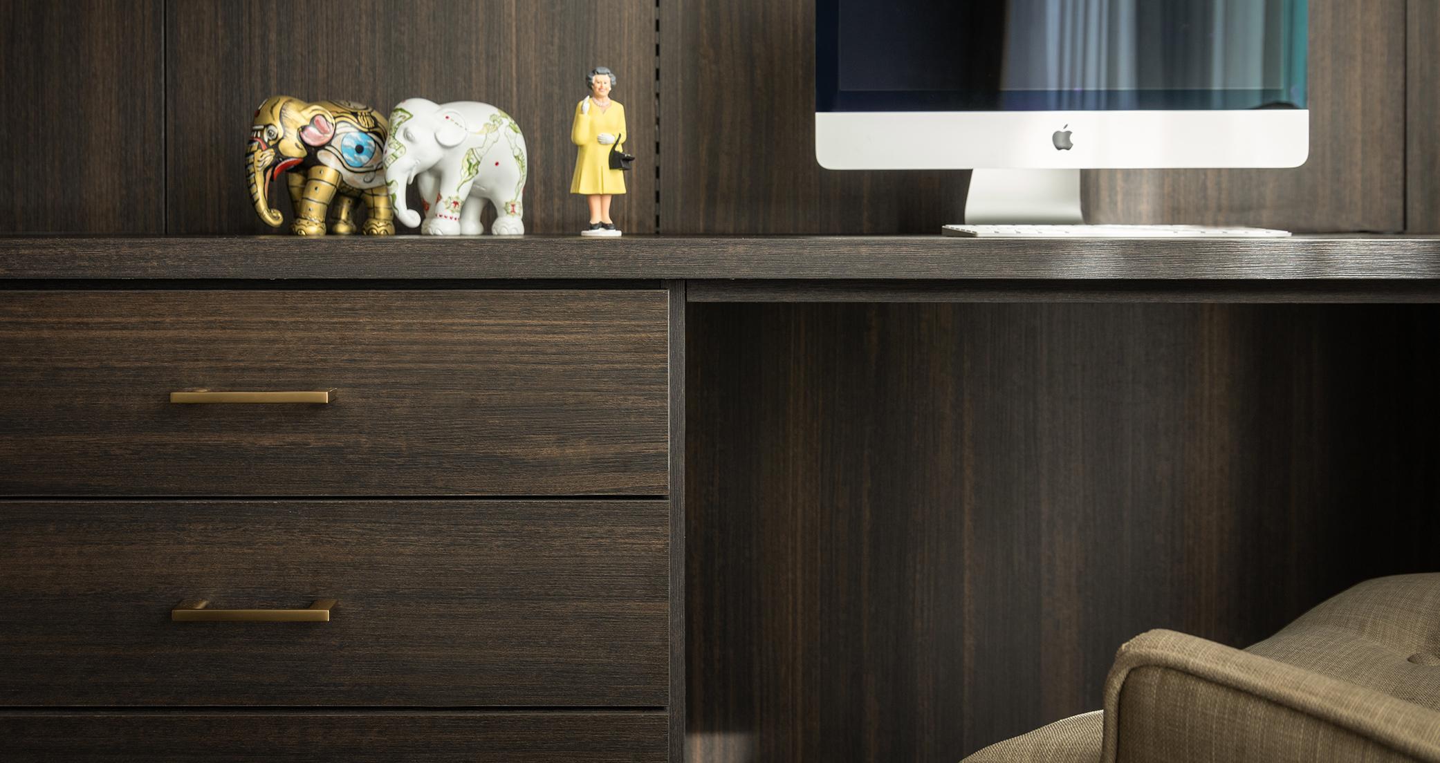 "Oficina en casa con acabado de madera oscura, cajones de escritorio con herrajes dorados e iluminación LED creada por California Closets
"