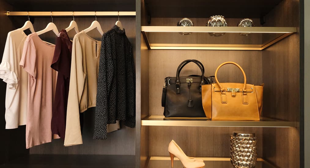 Dark wood custom closet featuring display shelves illuminated by energy-efficient integrated LED lighting