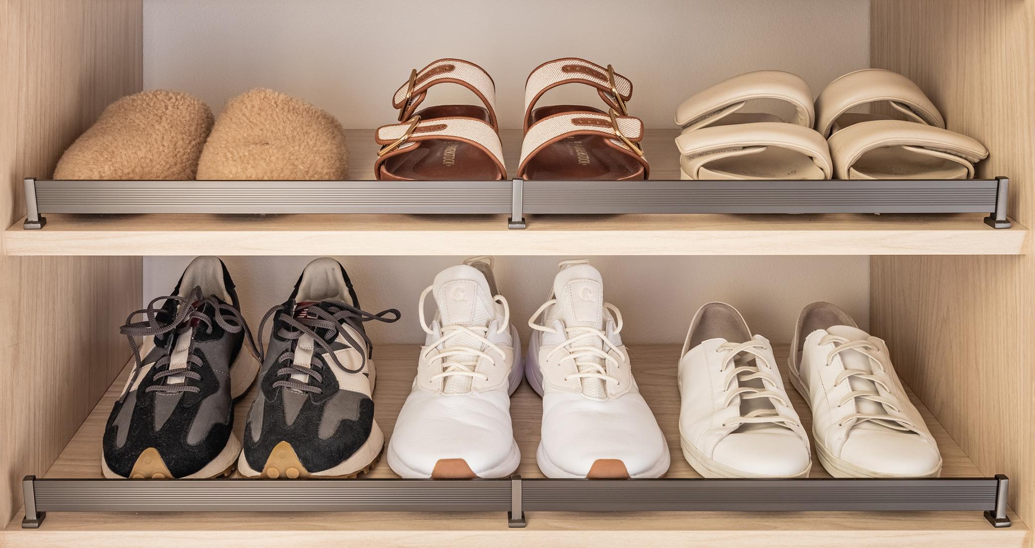 Shoe storage with metal shoe fence and tilted shelves in a custom walk in closet in a light wood grain finish by California Closets