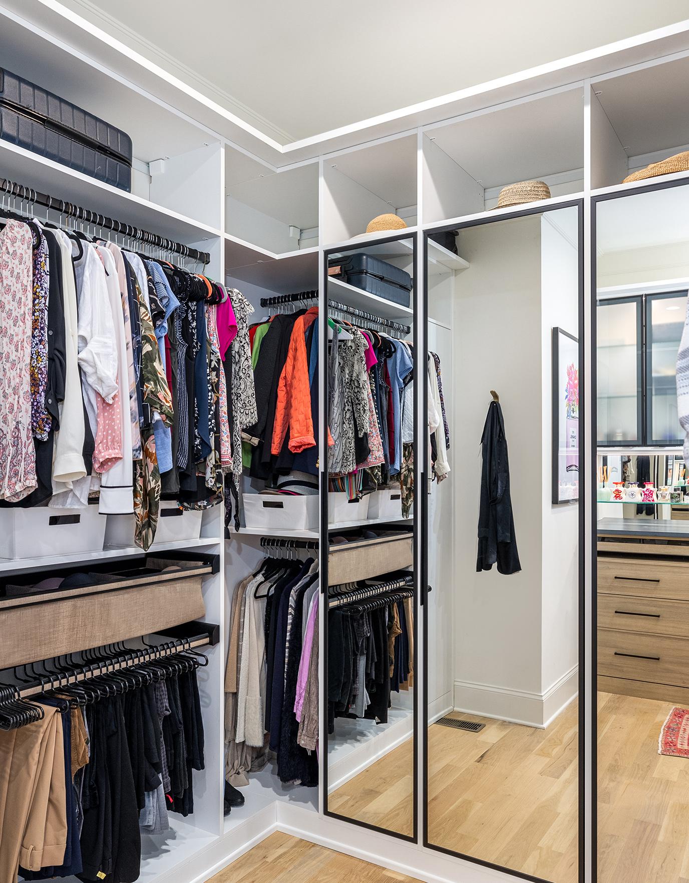 Her walk in closet with open shelves and mirrored doors in white wood grain finish created by California Closets