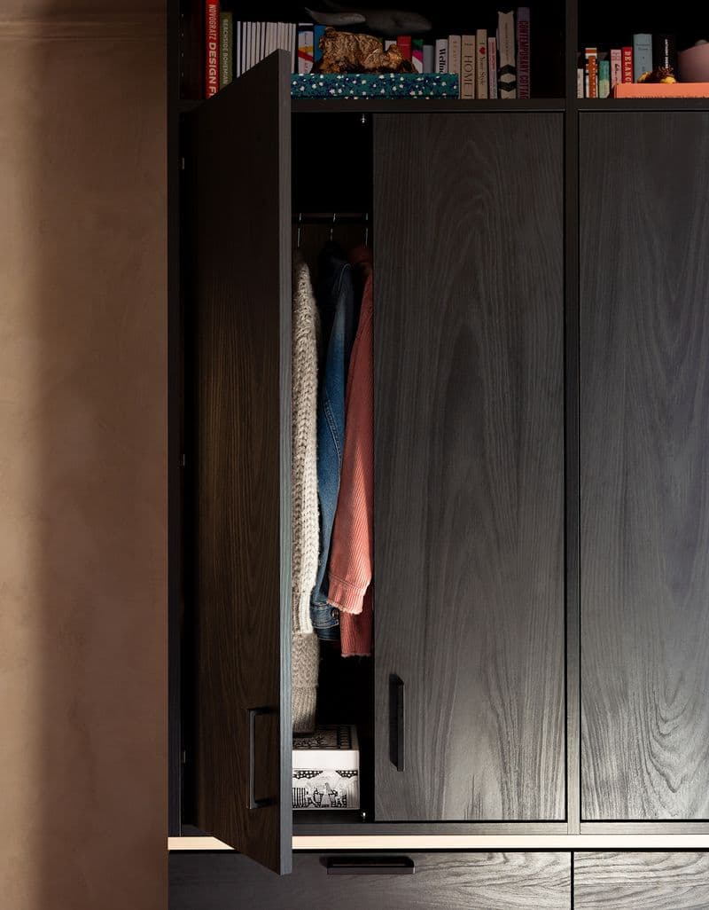 Closet doors opened to show clothes with curio shelves above in dark wood grain finish by California Closets