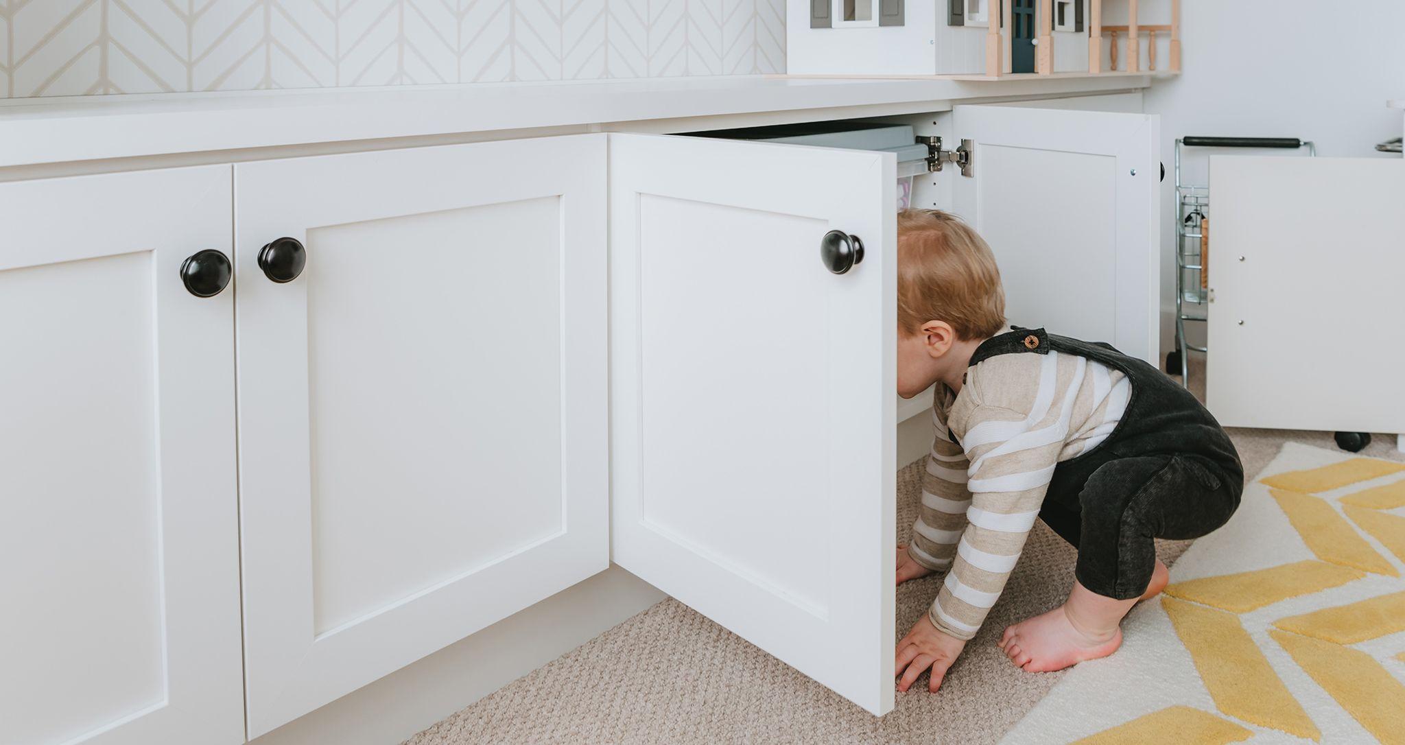 Child playing in custom playroom with toy storage cabinets opened by California Closets