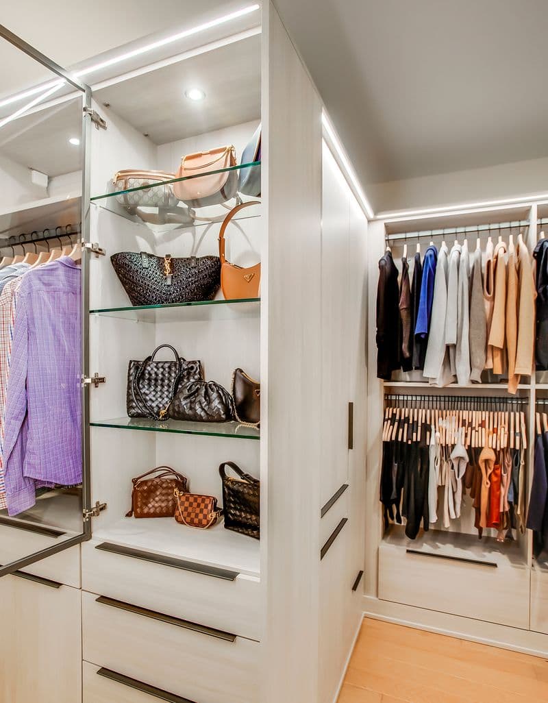 Estantes de vidrio en un armario para caminar para almacenar bolsos con iluminación LED creada por California Closets