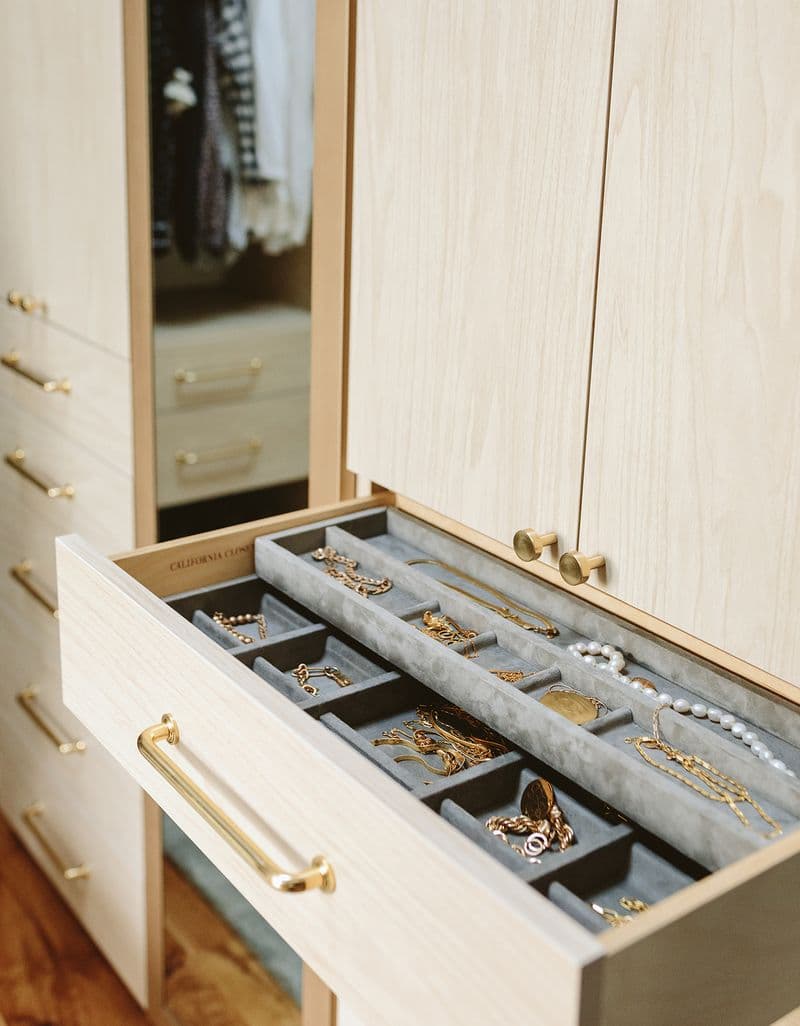 Cajón de armario para joyas y accesorios con herrajes en tono dorado y acabado en madera clara de California Closets