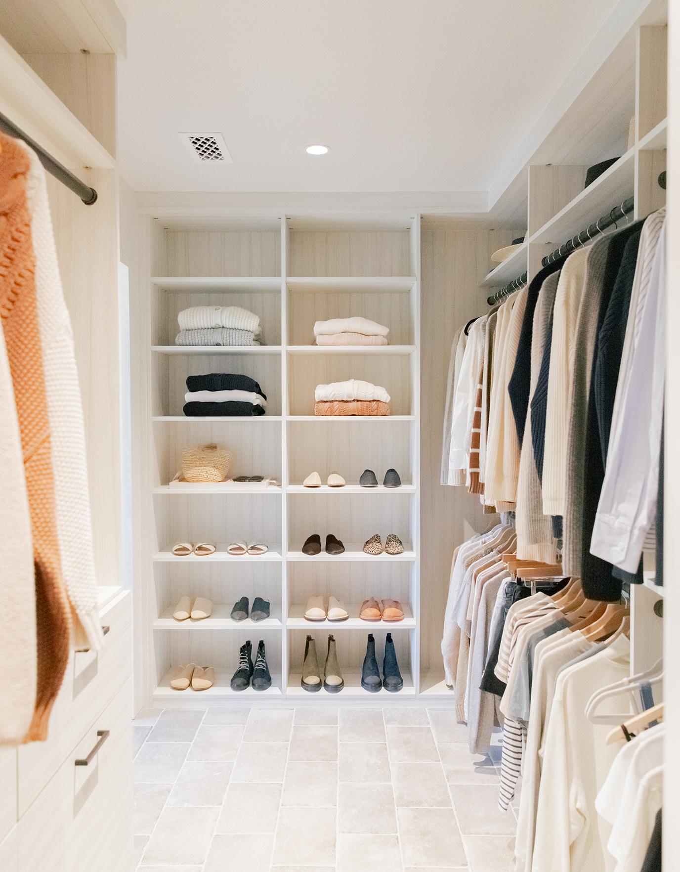 Custom walk in closet organization for sweaters, shoes and hanging clothes in a neutral wood grain finish by California Closets