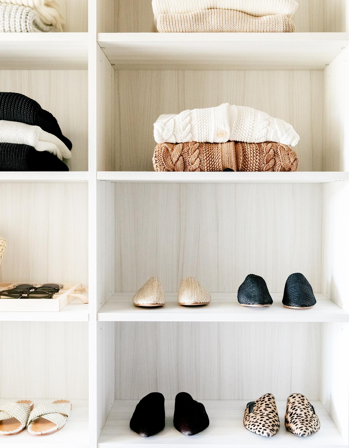 Walk in closet with custom shelving for shoes and sweaters in a neutral wood grain finish by California Closets