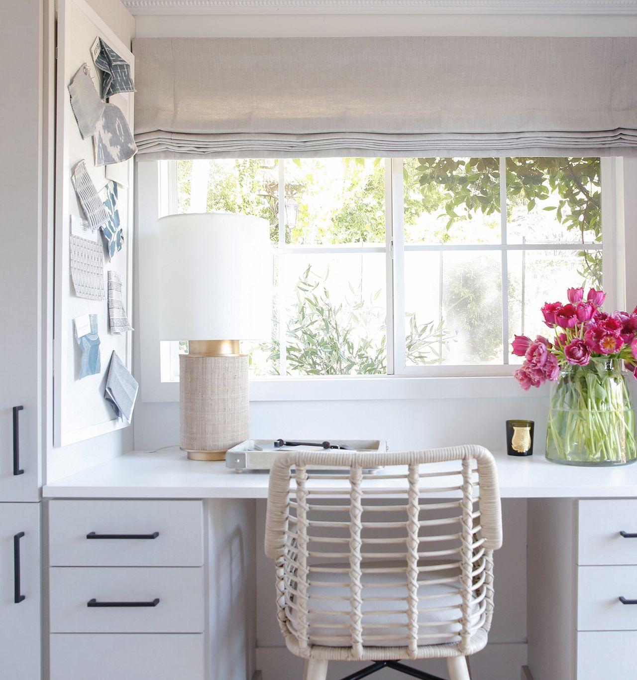 Home office workspace with cabinets, drawers, and a storage system below a window view created by California Closets