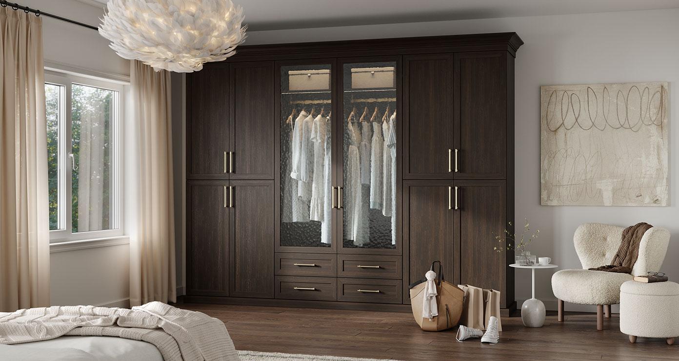 Wardrobe closet finished in dark wood grain with glass door cabinets and drawers by California Closets