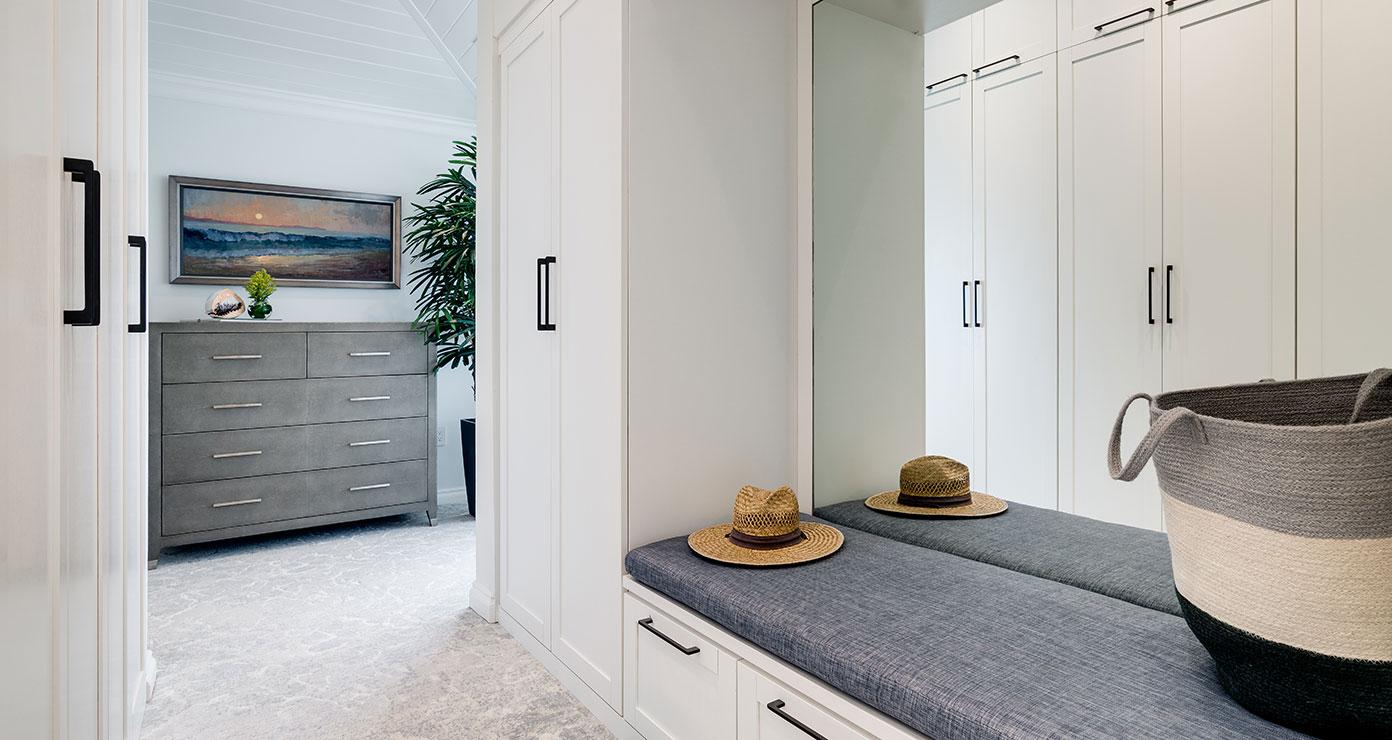 White matte cabinet storage with bench and mirrored wall in hallway by California Closets