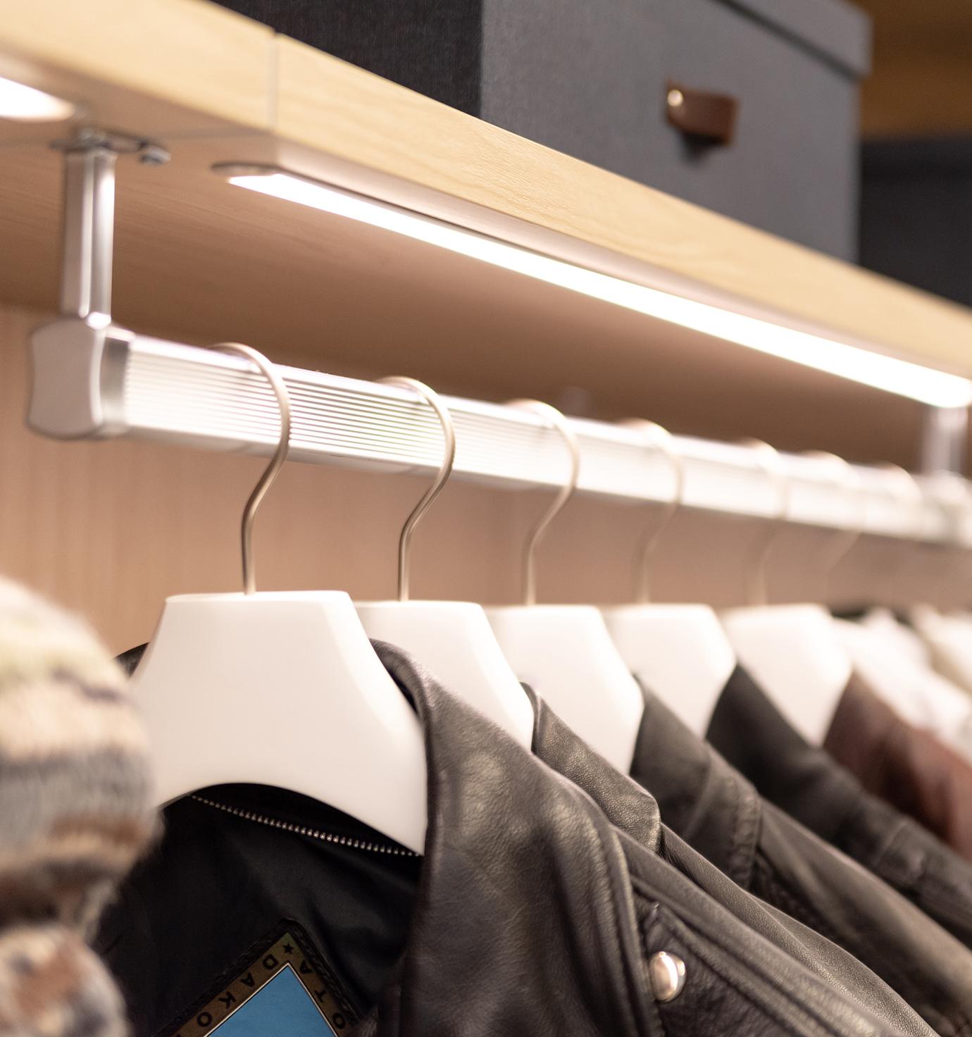 Iluminación de armario con barra para ropa con acabado de madera clara y estantes abiertos de California Closets