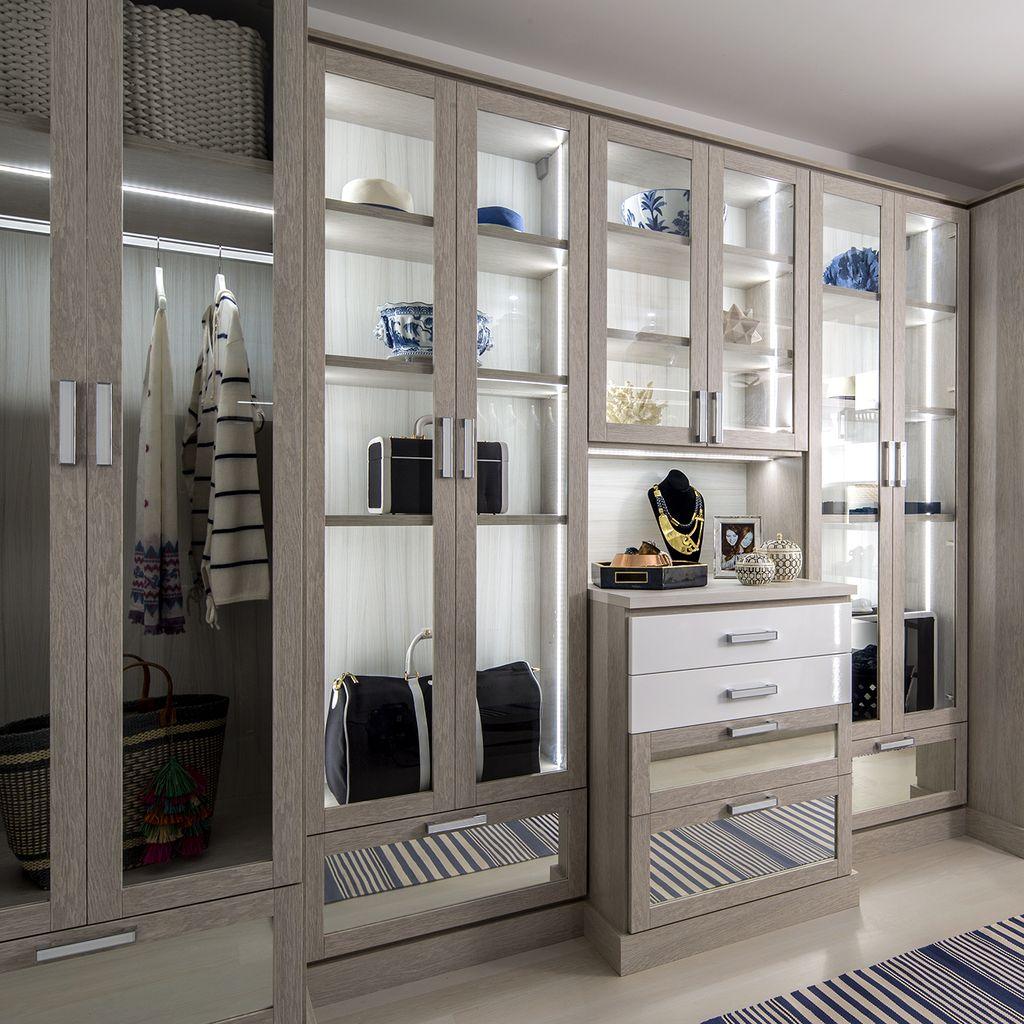 Closet designed with wardrobe cabinet glass doors and lighting by California Closets