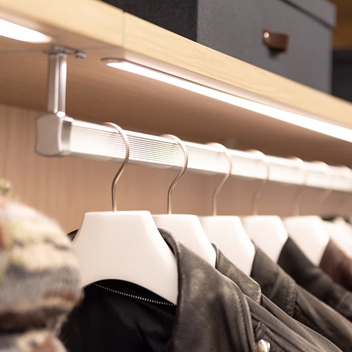 Iluminación LED en cinta personalizada sobre la barra para colgar ropa en vestidor por California Closets