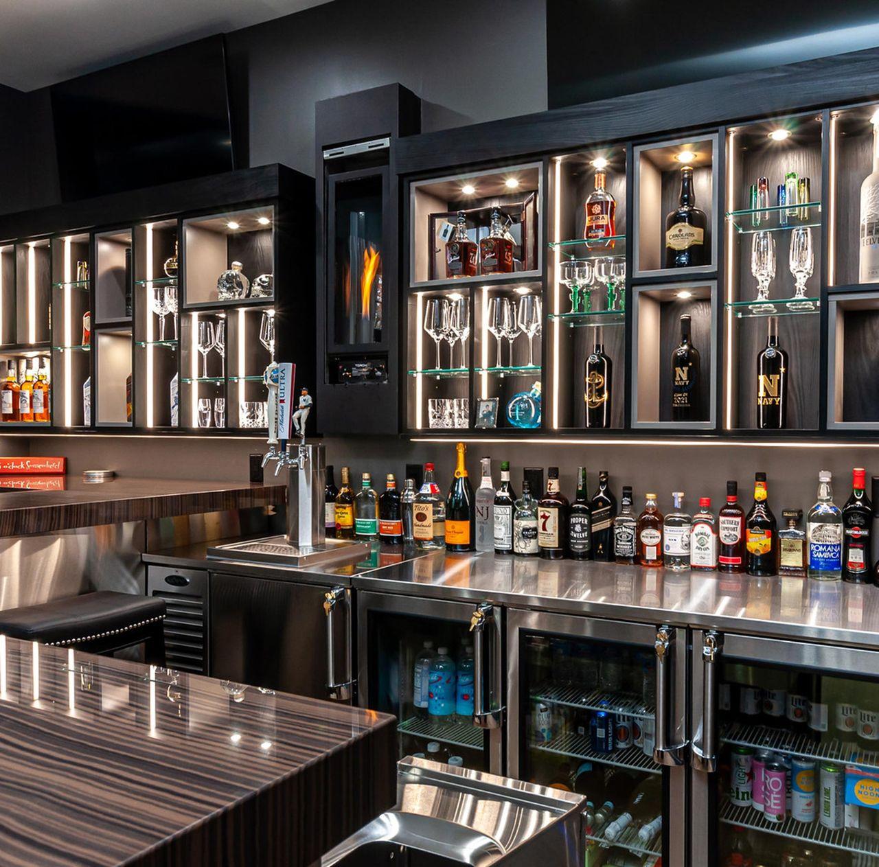 Luxe home bar design with custom counterspace, open lighted shelving and glass cabinet doors by California Closets