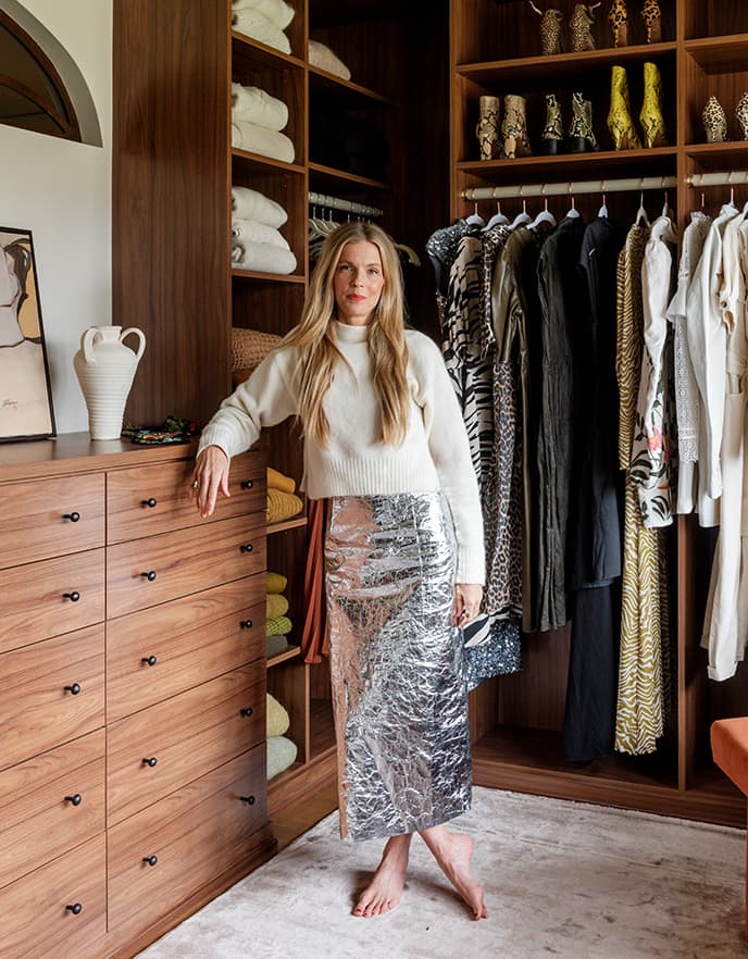 Designer Sarah Sherman Samuel standing in her walk in closet leaning against siena-finished built in dresser drawers from California Closets