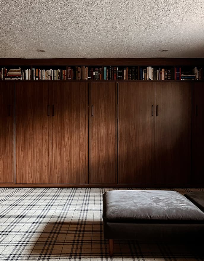 Cama abatible con acabado en madera oscura, mostrada cerrada con repisas para libros en la parte superior, de California Closets