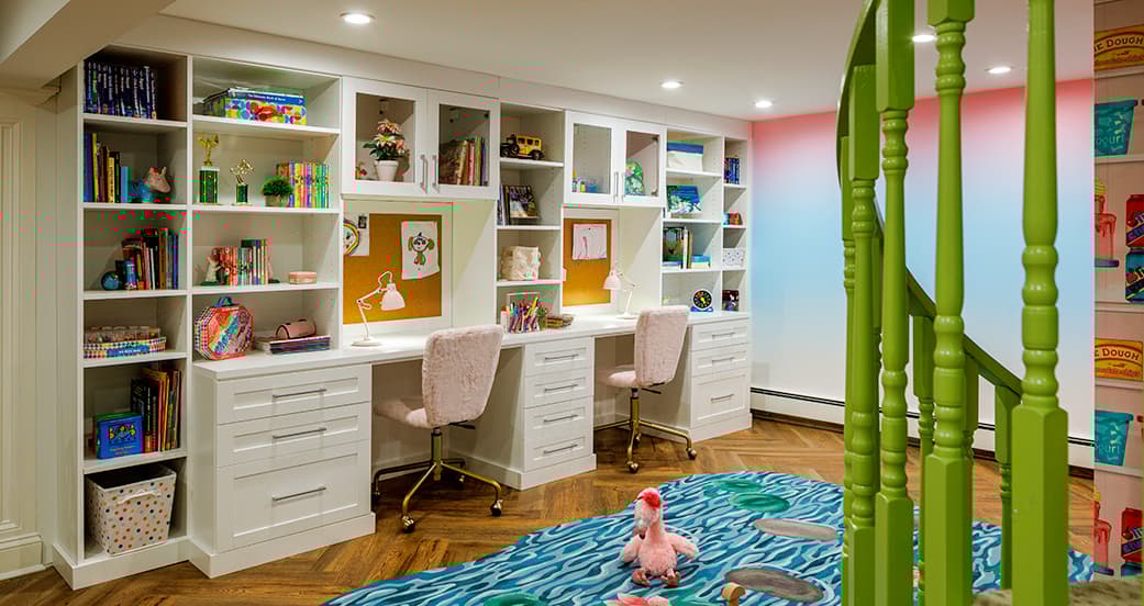 Built‑in homework station with twin desks and bookcase storage in a playroom, crafted by California Closets