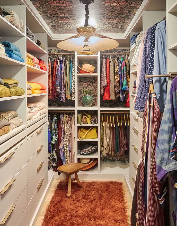 Walk in closet with crafts inspired wallpaper and white shelving by California Closets