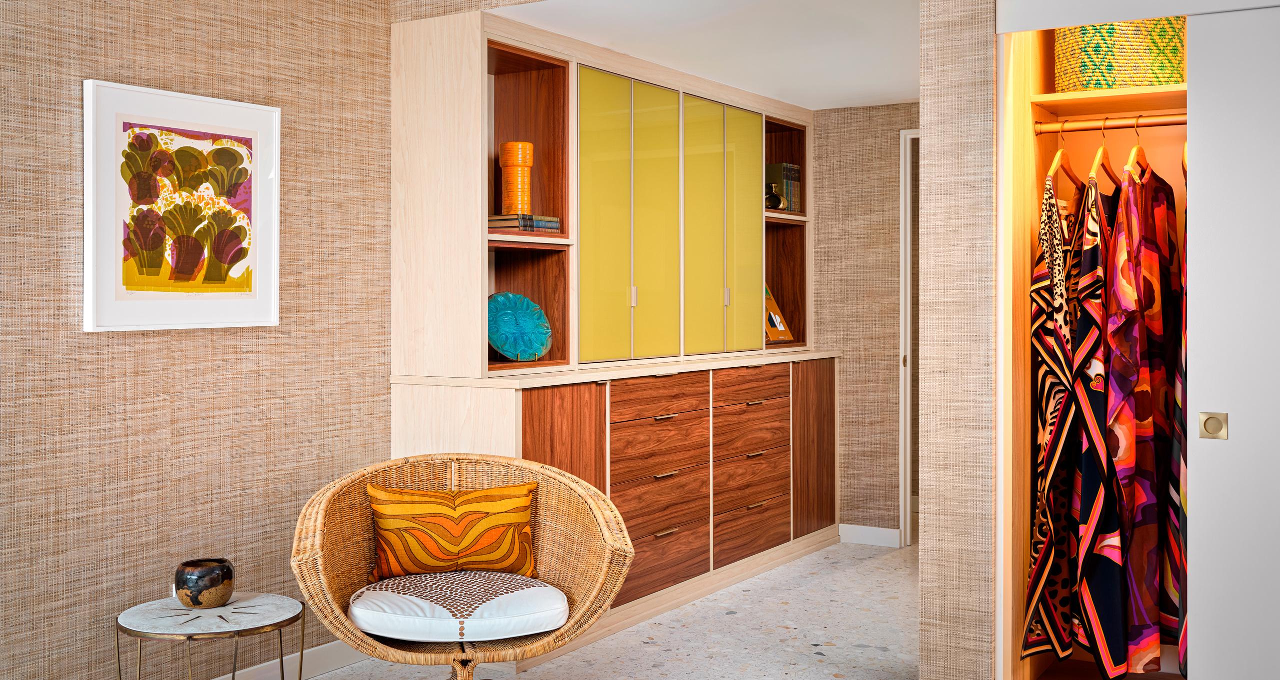 Custom midcentury modern closet and wardrobe with yellow glass doors, walnut cabinetry, and open shelving in Trina Turk’s Palm Springs home, featuring colorful caftans and retro decor.