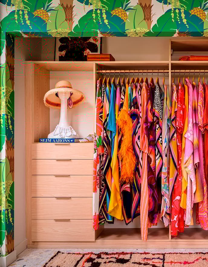 Custom closet system surrounded by palm wallpaper, open shelving and drawers and vibrantly colored wardrobe in Trina Turk’s Palm Springs home.