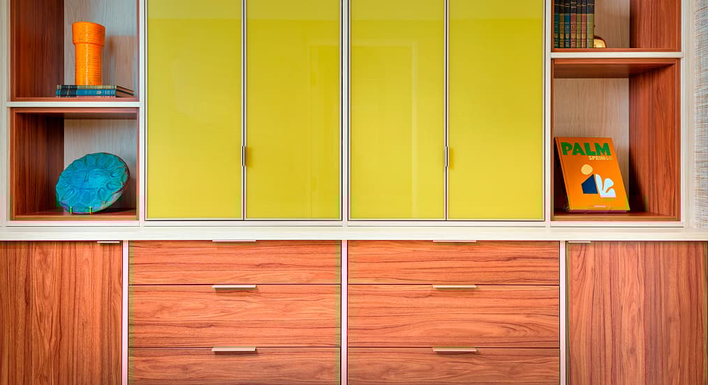 Gabinete empotrado personalizado para ropa blanca con acabado en nogal, puertas superiores de vidrio amarillo y estantes abiertos con decoración retro en la casa moderna de mediados de siglo de Trina Turk en Palm Springs.