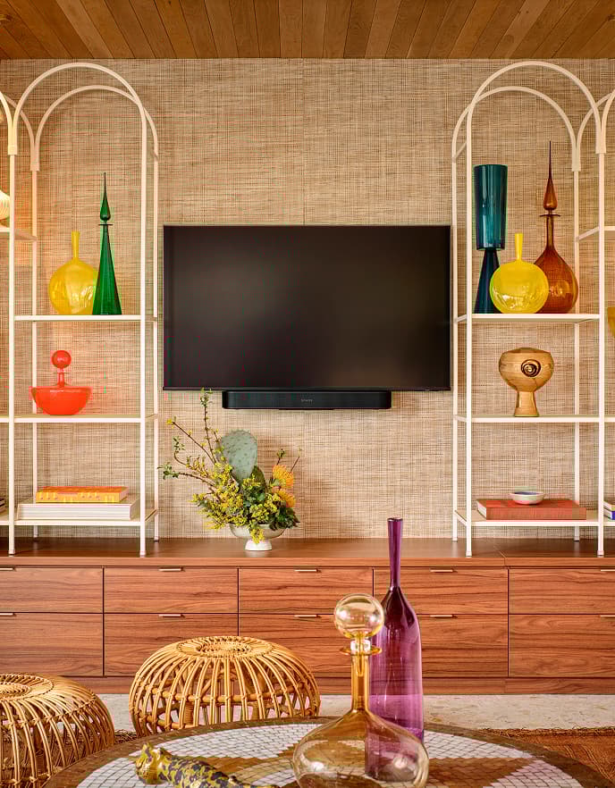 Centro multimedia empotrado con étagères arqueadas vintage, decoración de vidrio colorido y detalles tejidos en la sala moderna de mediados de siglo de Trina Turk en Palm Springs.