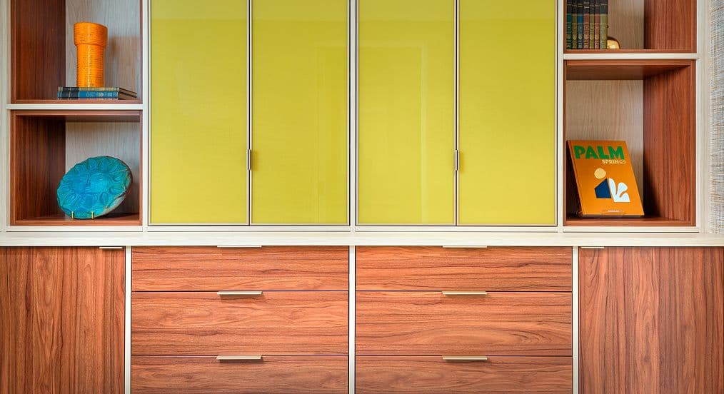 Primer plano de una unidad de pared personalizada de estilo moderno de mediados de siglo con cajones de madera cálida e insertos de puertas de vidrio pintado por detrás en amarillo vibrante con marcos de aluminio.