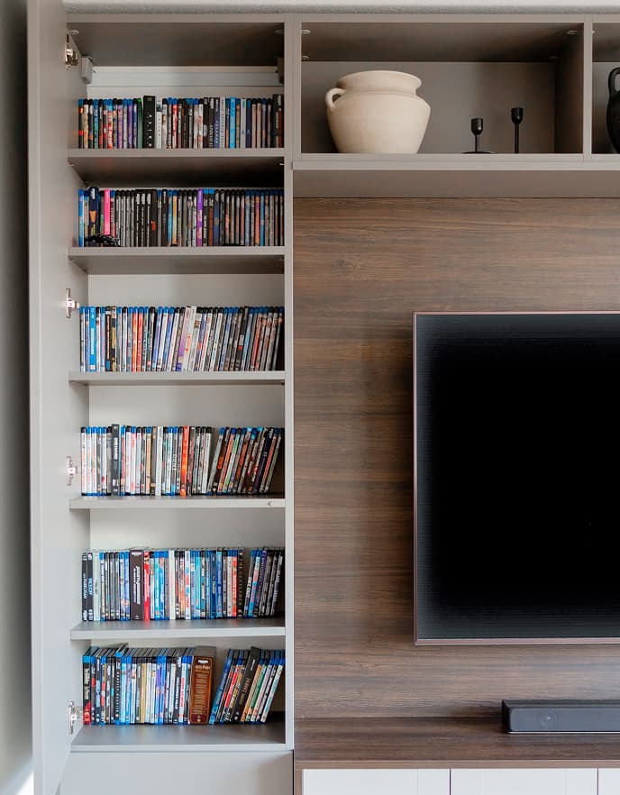 Smart living room organization by California Closets highlighting hidden media storage shelves within a custom built-in entertainment unit.