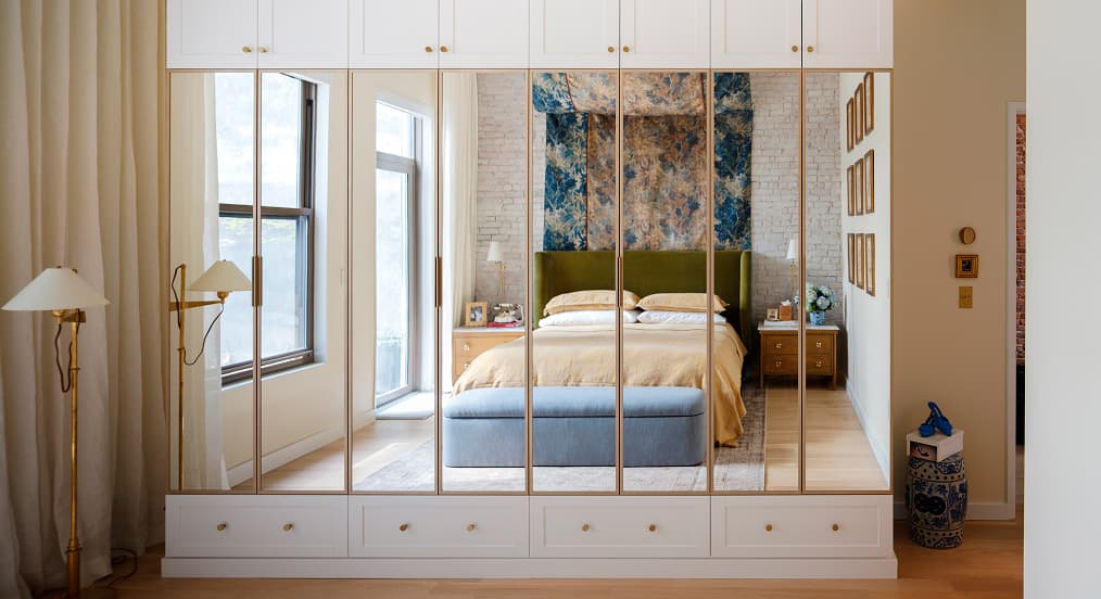 Modern bedroom wall unit featuring built-in storage drawers and seamlessly integrated mirrored closet doors designed by California Closets.