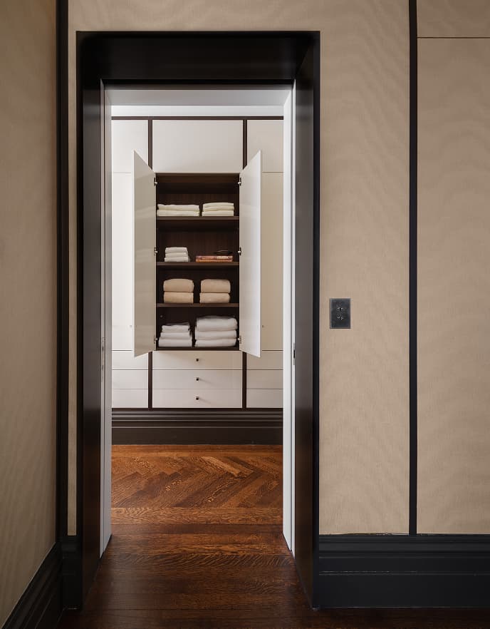 Clóset personalizado para ropa de cama de California Closets con puertas de gabinete blancas abiertas, repisas de madera oscura y toallas dobladas California Closets