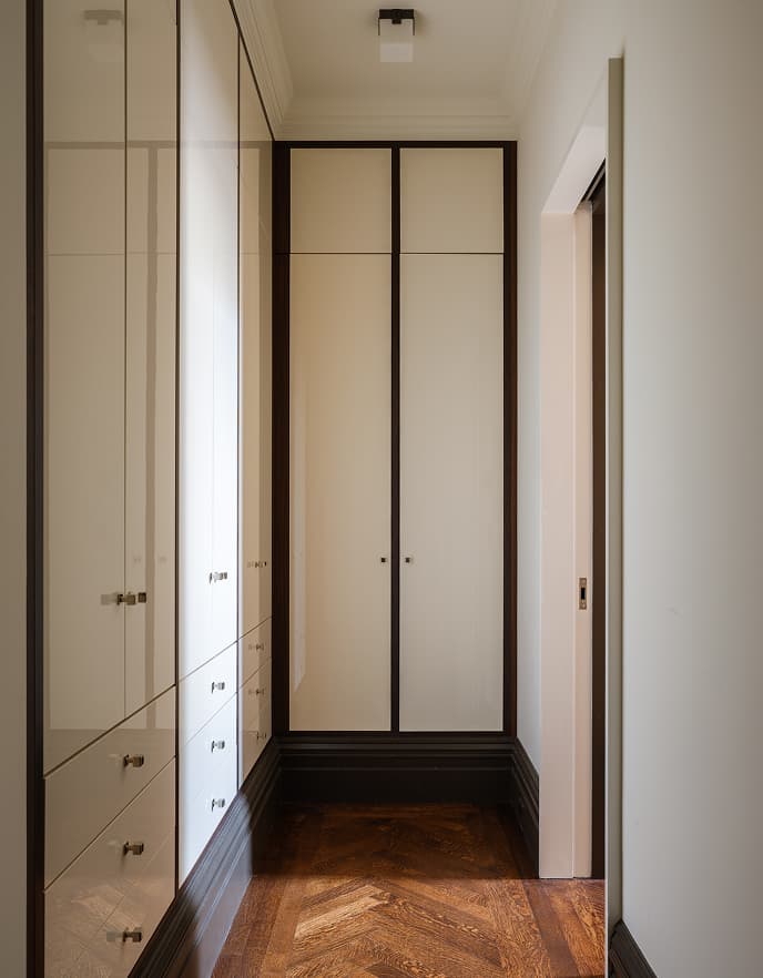 Custom built-in wardrobes with gloss cream doors, dark trim, and herringbone floors by California Closets.