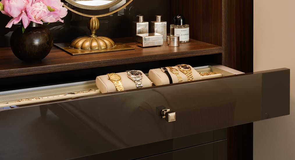Open velvet-lined jewelry drawer with custom watch storage pillows and dark wood shelving by California Closets.