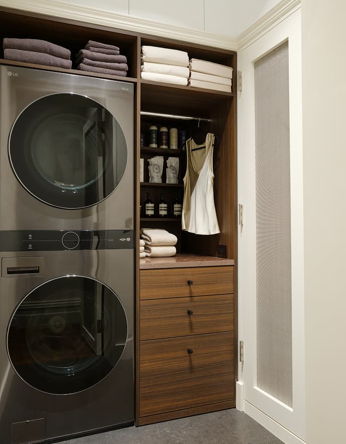 Custom wood laundry cabinets, shelving, and drawers next to a stacked washer and dryer by California Closets.