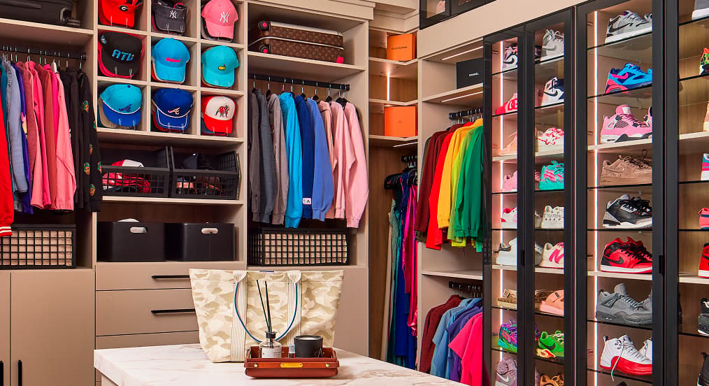 Custom walk-in closet featuring hat cubbies, hanging storage, and a sneaker display wall by California Closets