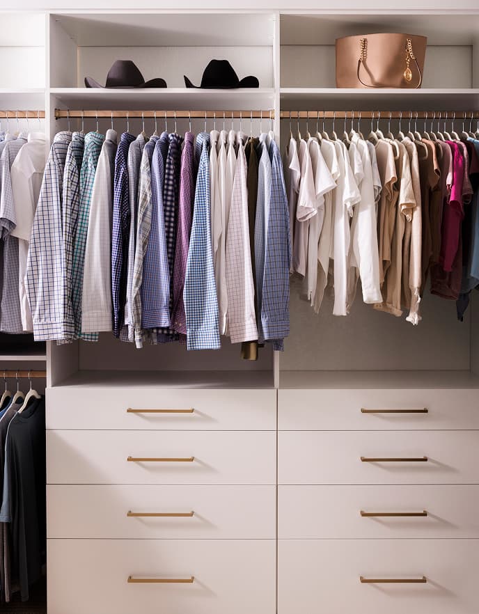 Custom white walk-in closet with built-in drawers, gold hardware, and organized hanging storage by California Closets