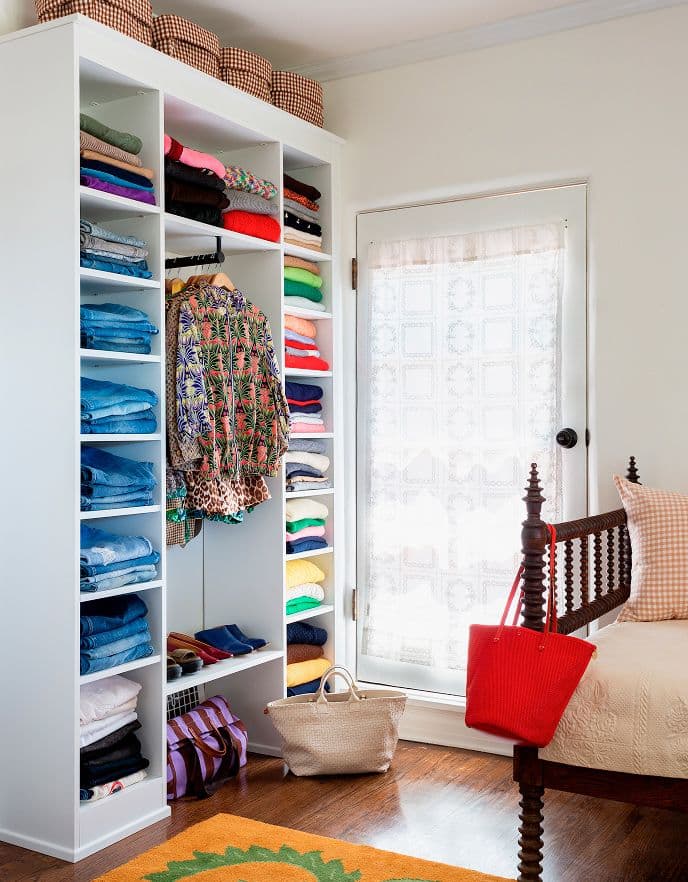 Estantes abiertos de piso a techo junto a una cama vintage en una luminosa habitación de huéspedes de California Closets