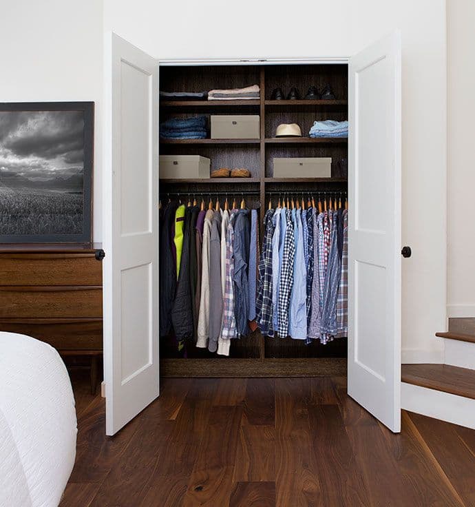 Bedroom reach in closet with built-in shelves in dark wood finish with white doors by California Closets