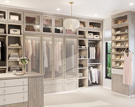 Diseño de vestidor personalizado con estantes adicionales, espacio para guardar zapatos, isla y vitrinas iluminadas de California Closets